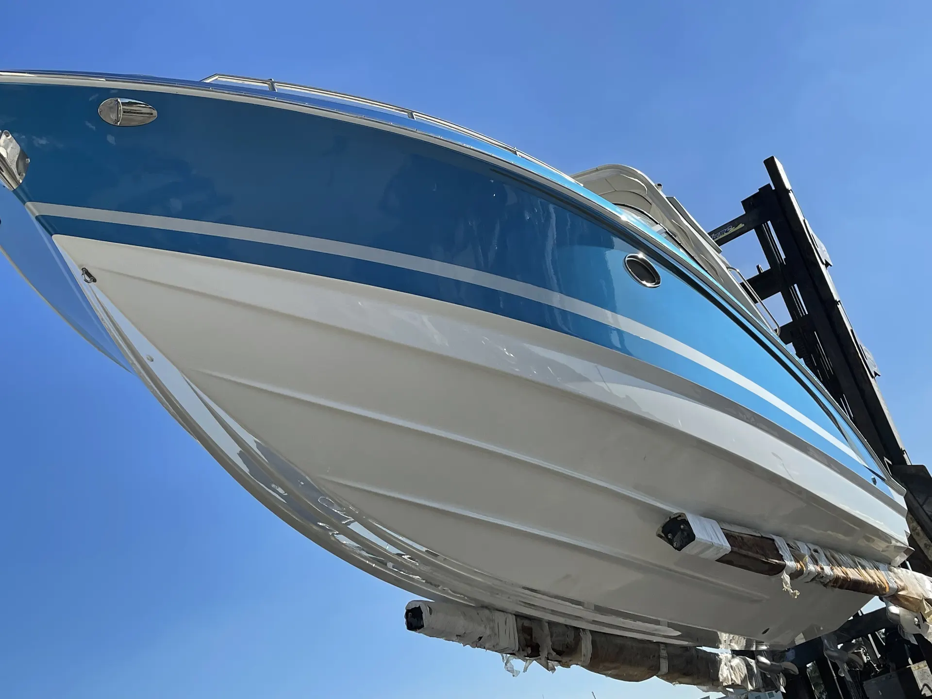 Completed powerboat hull with a glossy refinishing coat while supported in a yard forklift