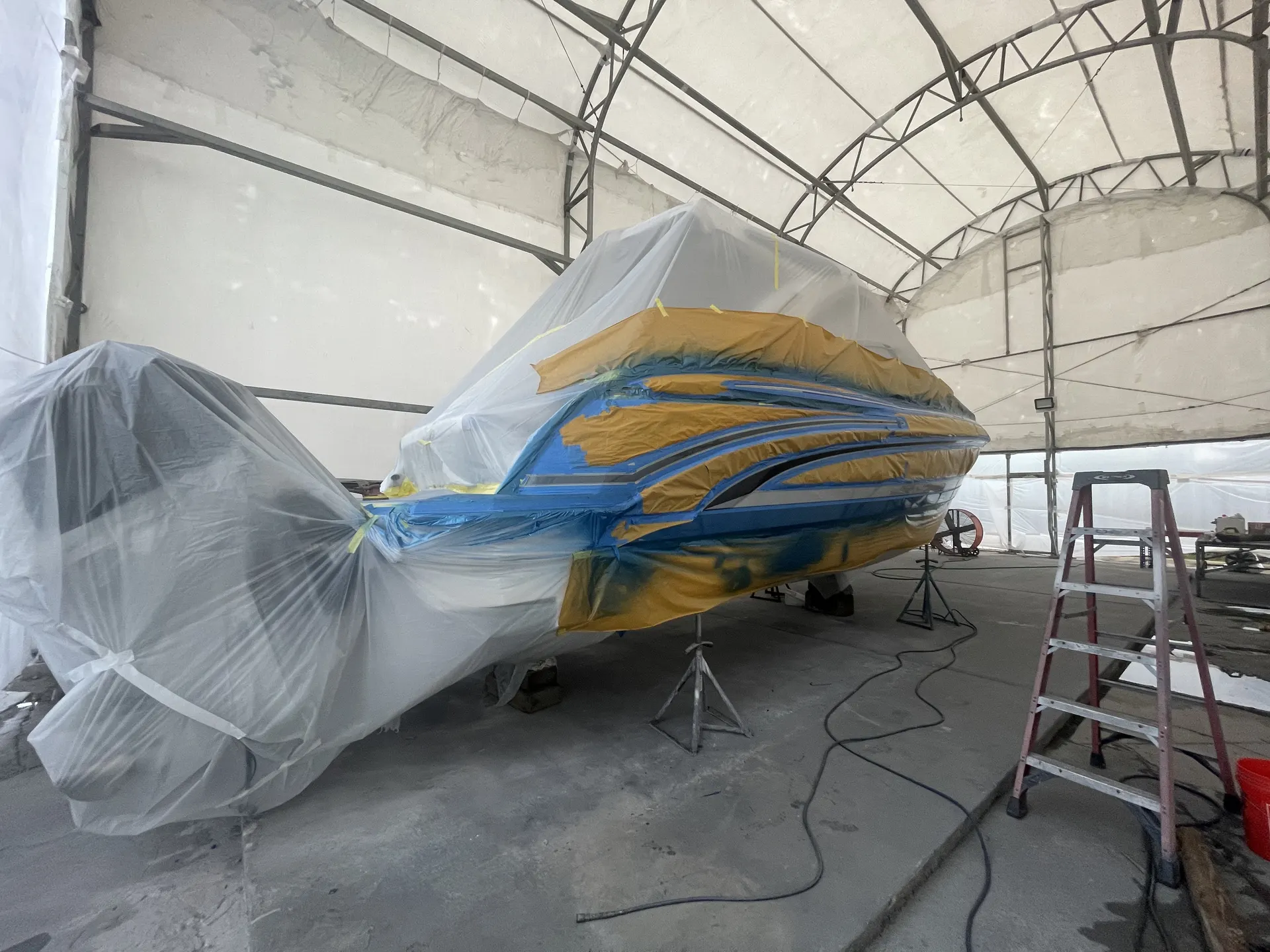 Stern-quarter view of a powerboat under plastic and tape masking during refinishing