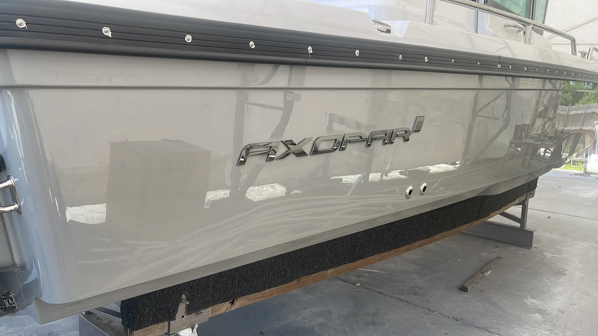 Axopar hull side with raised lettering and a high-gloss grey finish in a marine workshop