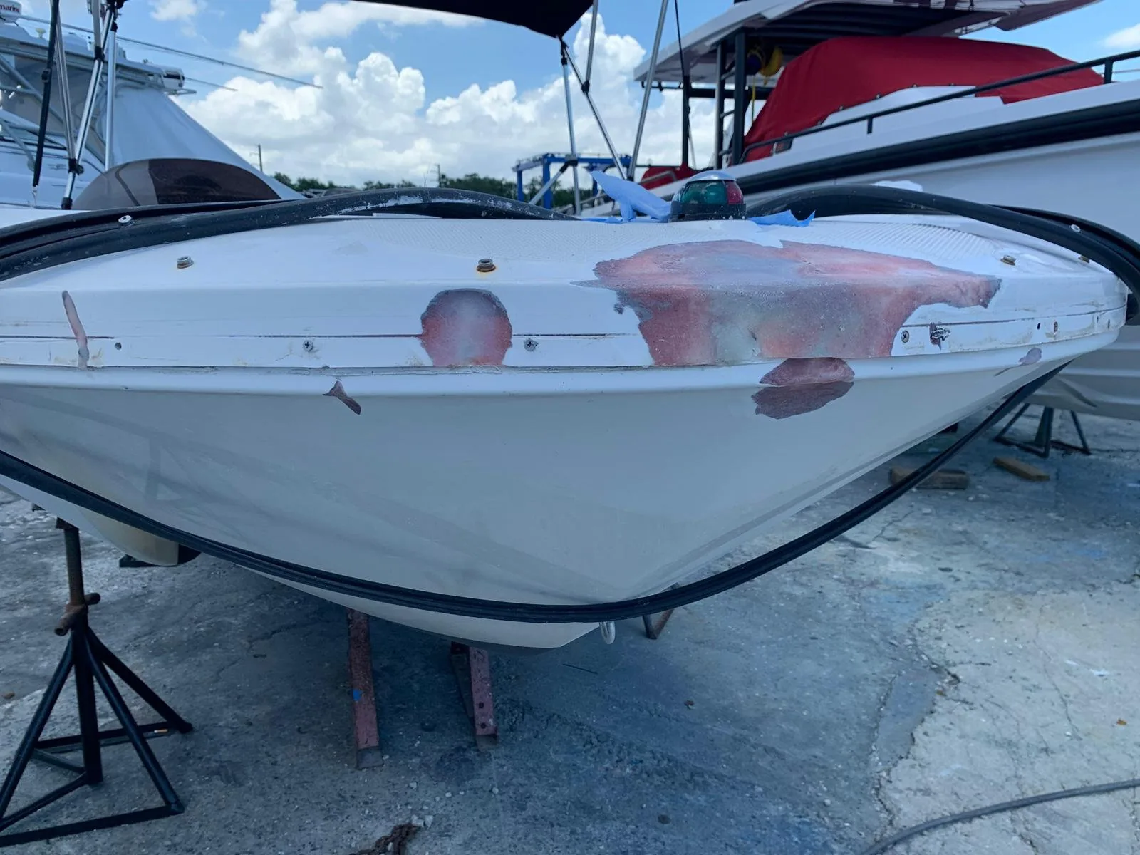 Bow tip mid-repair with fairing compound patches and a loose rub rail in a boatyard