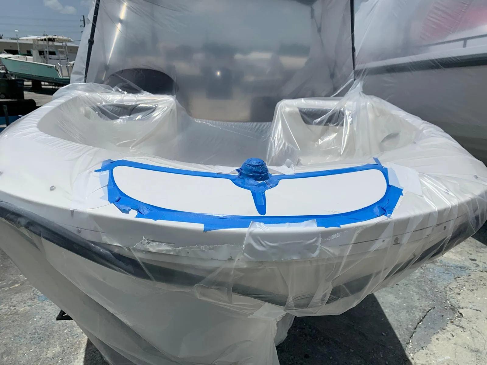 Bow tip masked with blue tape and plastic sheeting during marine coating preparation